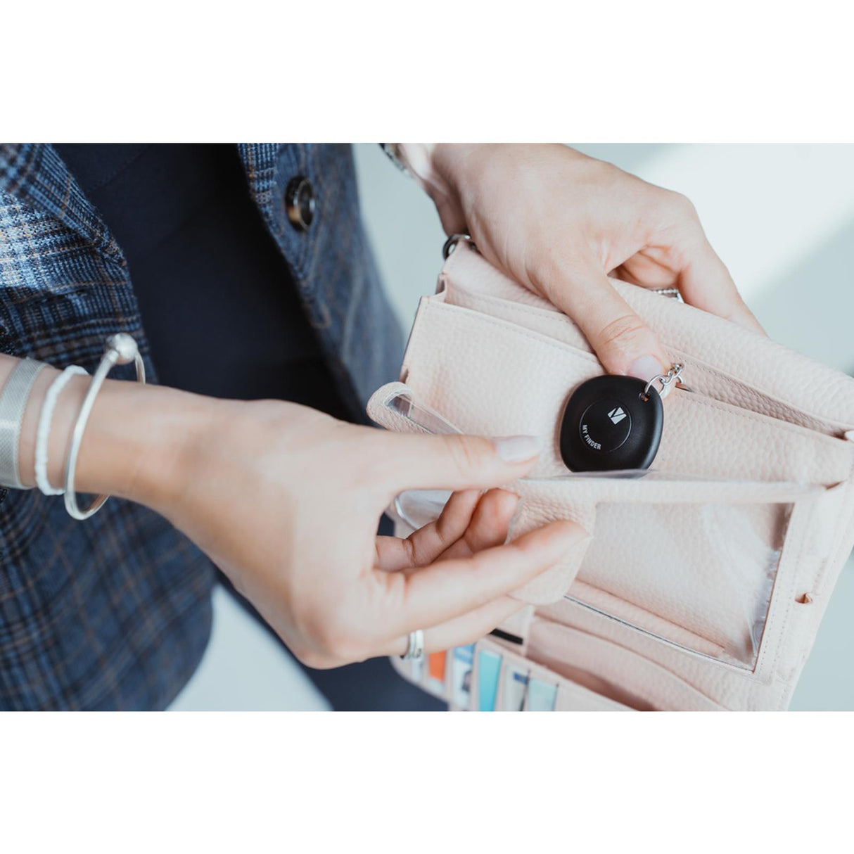 Nahaufnahme: Eine Person hält einen schwarzen, quadratischen Verbatim Bluetooth Tracker mit Schlüsselring über einer beigen.