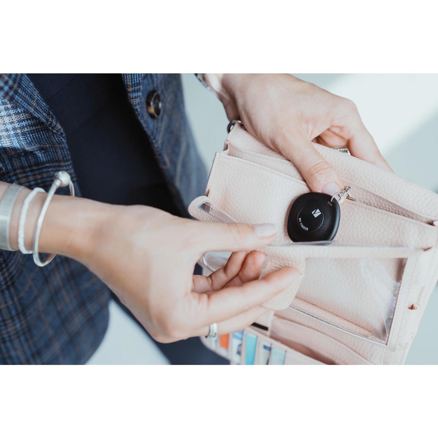 Nahaufnahme: Eine Person hält einen schwarzen, runden Verbatim Bluetooth Tracker mit Schlüsselring über einer hellrosa.