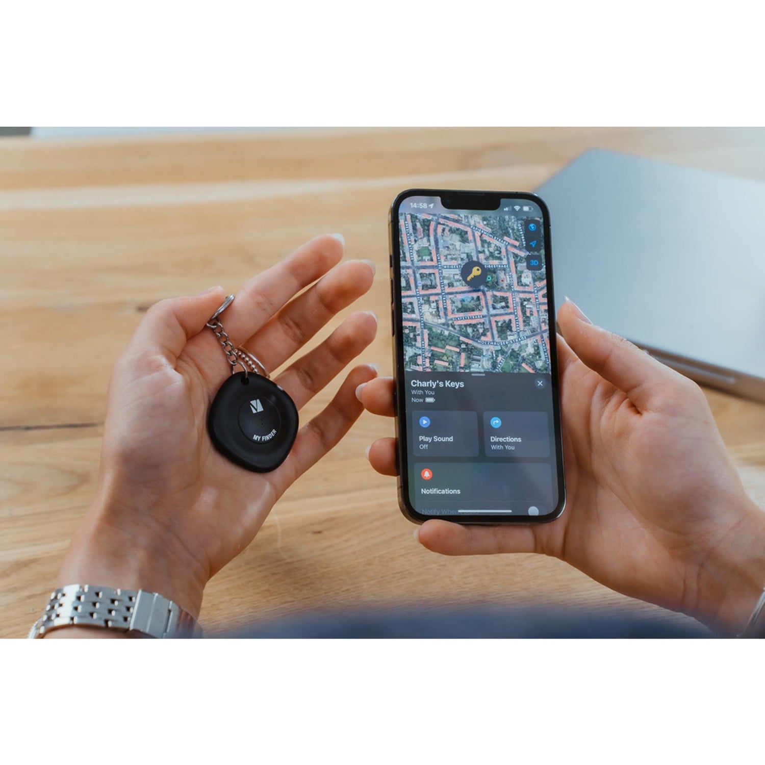 Hände halten schwarzen runden Verbatim Bluetooth Tracker und iPhone mit Karten-App, die den Tracker anzeigt.