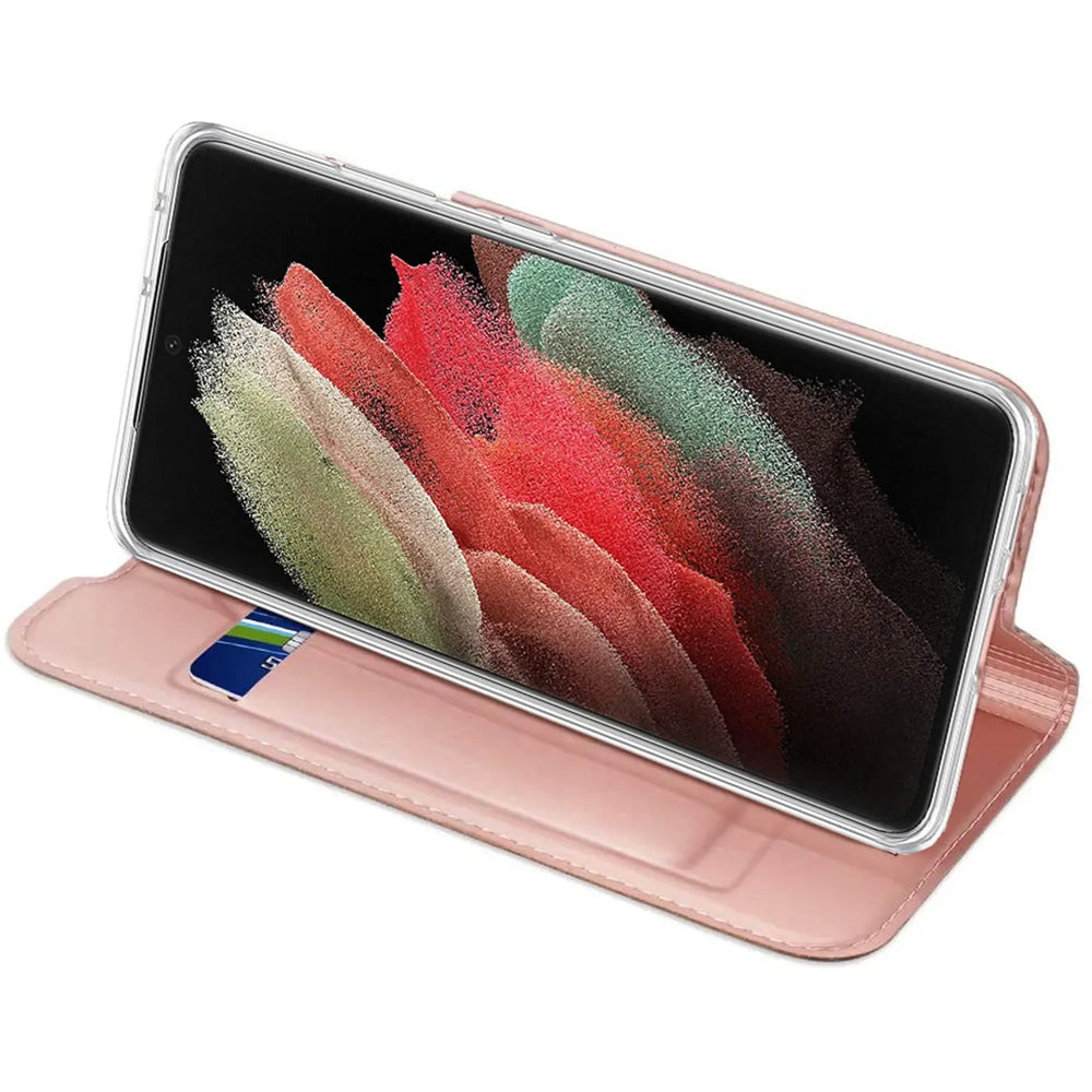 Samsung Galaxy S21 FE in roségoldener Metallic Flip Hülle aus Kunstleder, schräg von vorne, mit Kreditkarte.
