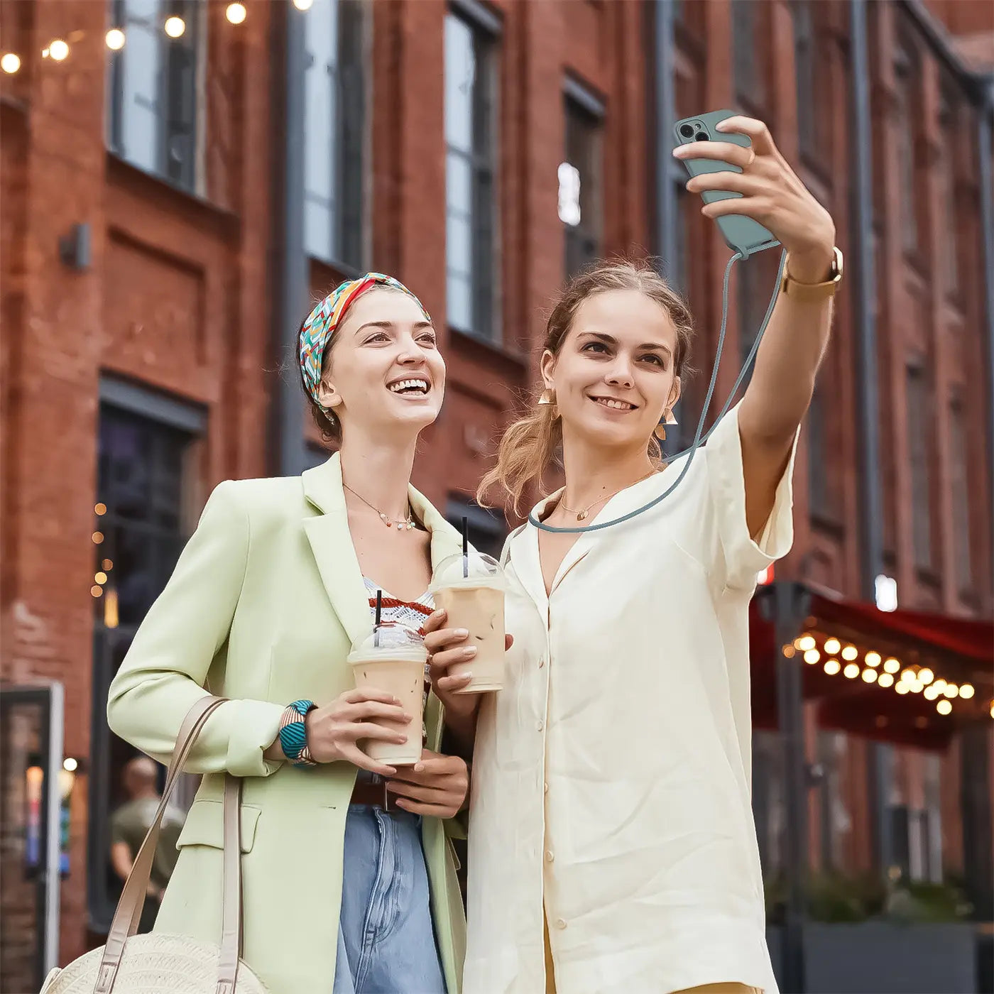 Zwei Frauen mit Kaffee, eine macht Selfie mit iPhone 16 mit Kette, von vorne