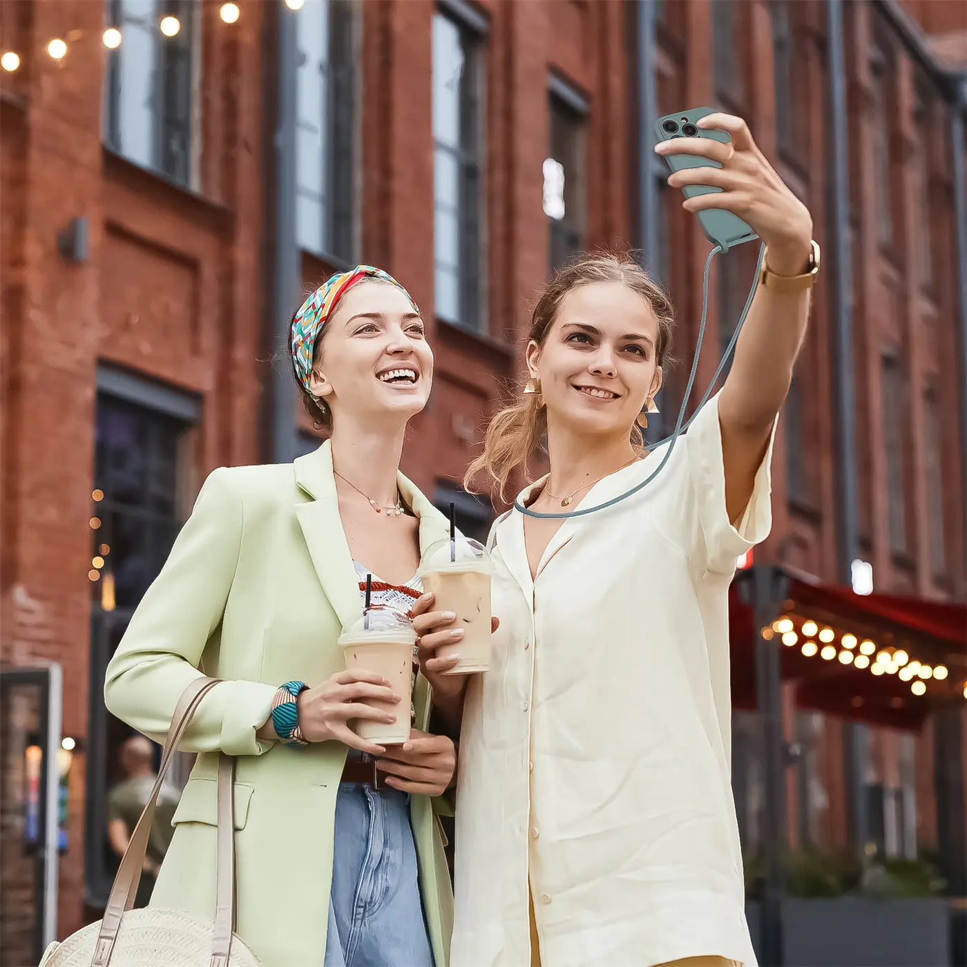Zwei Frauen mit Kaffee, eine hält ein hellblaues iPhone mit Kette.