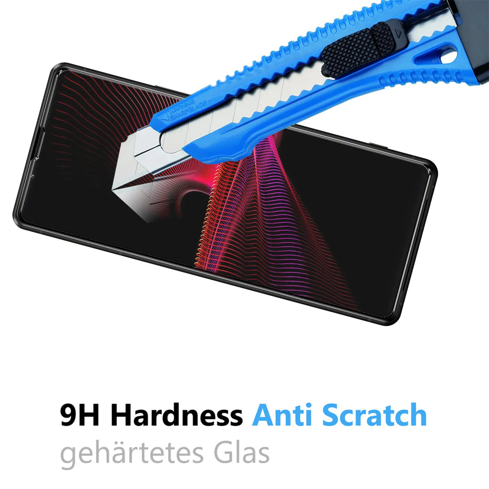 Blau-schwarzes Cuttermesser kratzt auf dem Displayschutz eines schwarzen Sony Xperia 1 V Smartphones, schräg von oben.