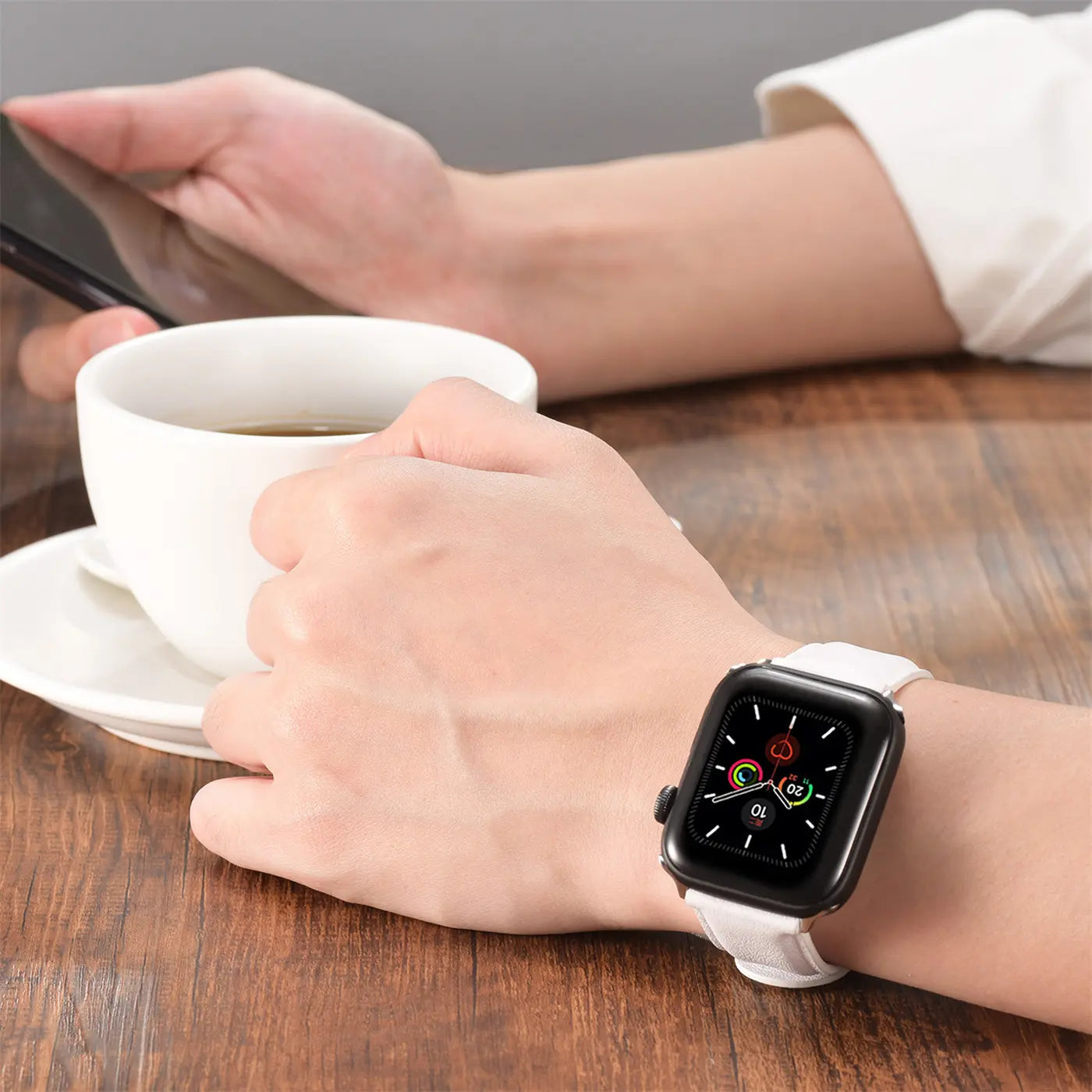 Weiße Leder Apple Watch mit schwarzem Gehäuse, von vorne, auf Hand mit Kaffeetasse.