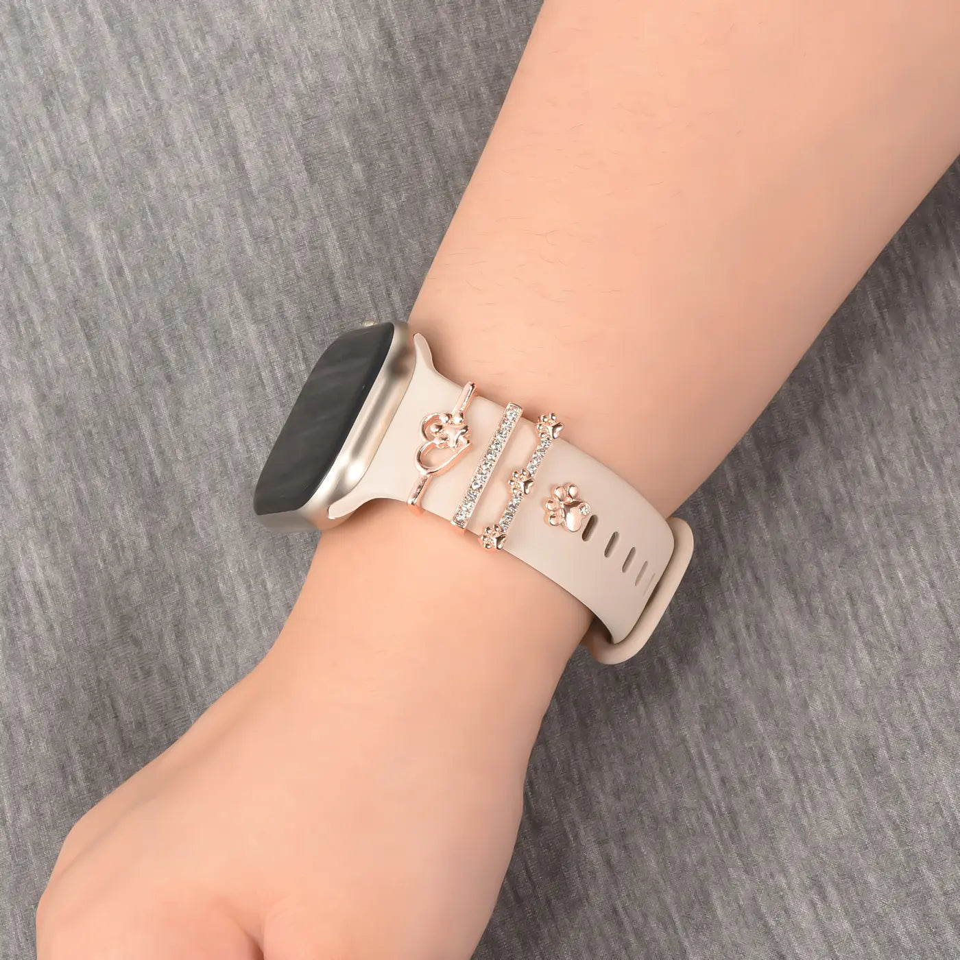 Beige Smartwatch-Armband mit roségoldenen Charms (Herz, Pfote) und Strasssteinen.