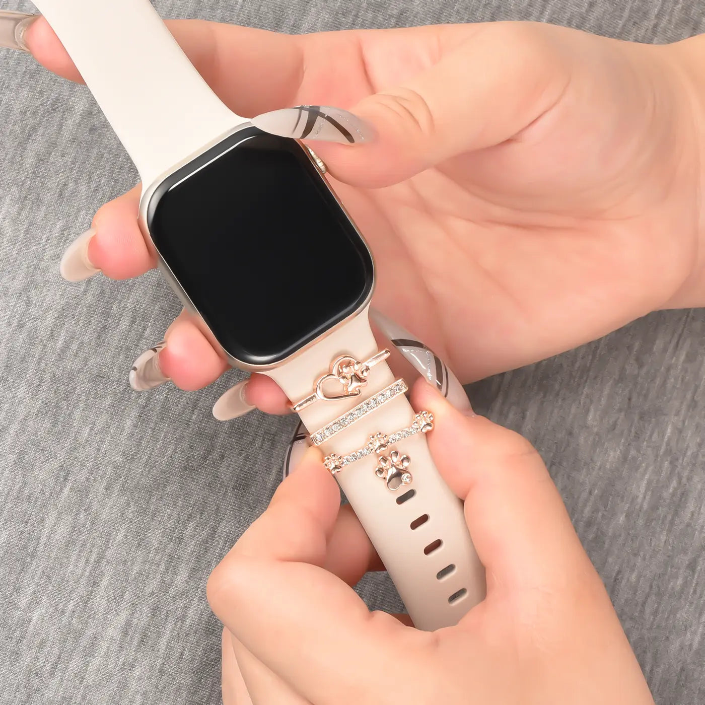 Smartwatch-Armband, beige, mit roséfarbenen Charms (Herz, Pfote), Nahaufnahme.