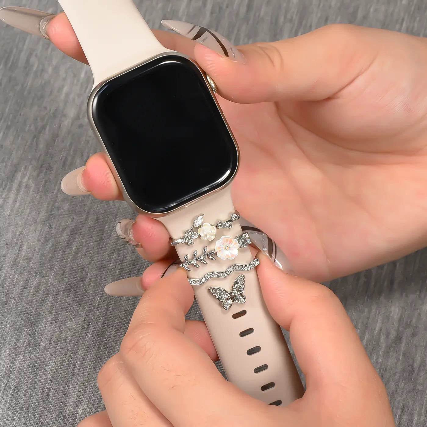 Beige Smartwatch-Armband mit silbernen Charms (Blumen, Schmetterling). Nahaufnahme.