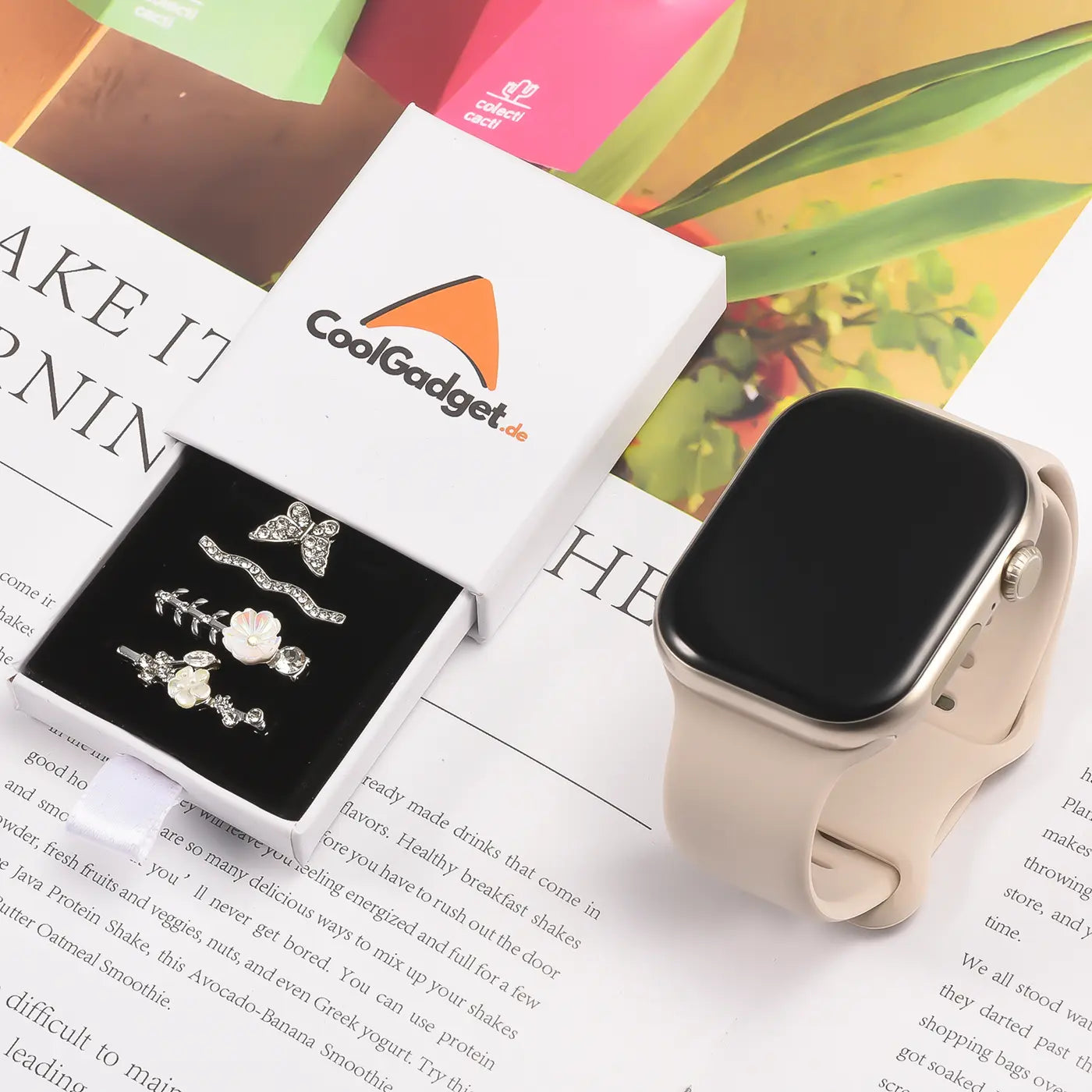 Silberfarbener Smartwatch-Schmuck mit Blumen- und Schmetterlings-Charms in geöffneter Box neben Smartwatch.