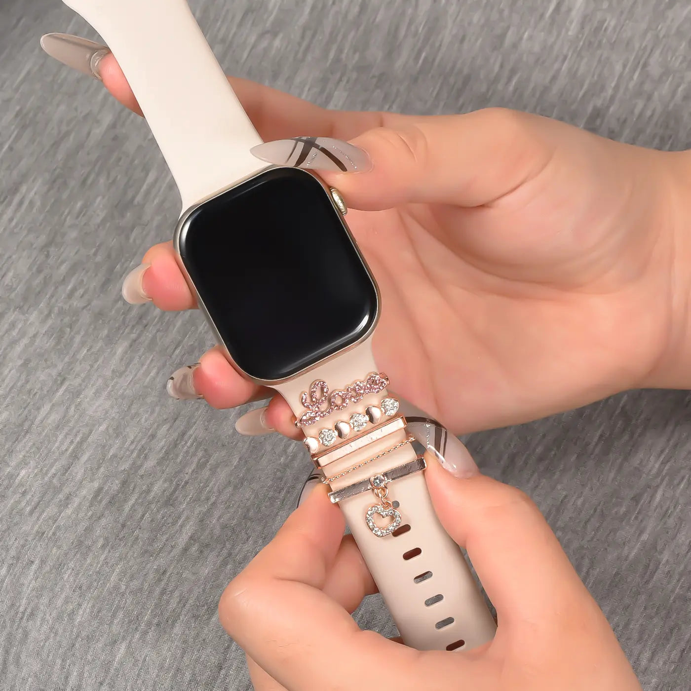 Hände schmücken helles Smartwatch-Armband mit roséfarbenen Charms.