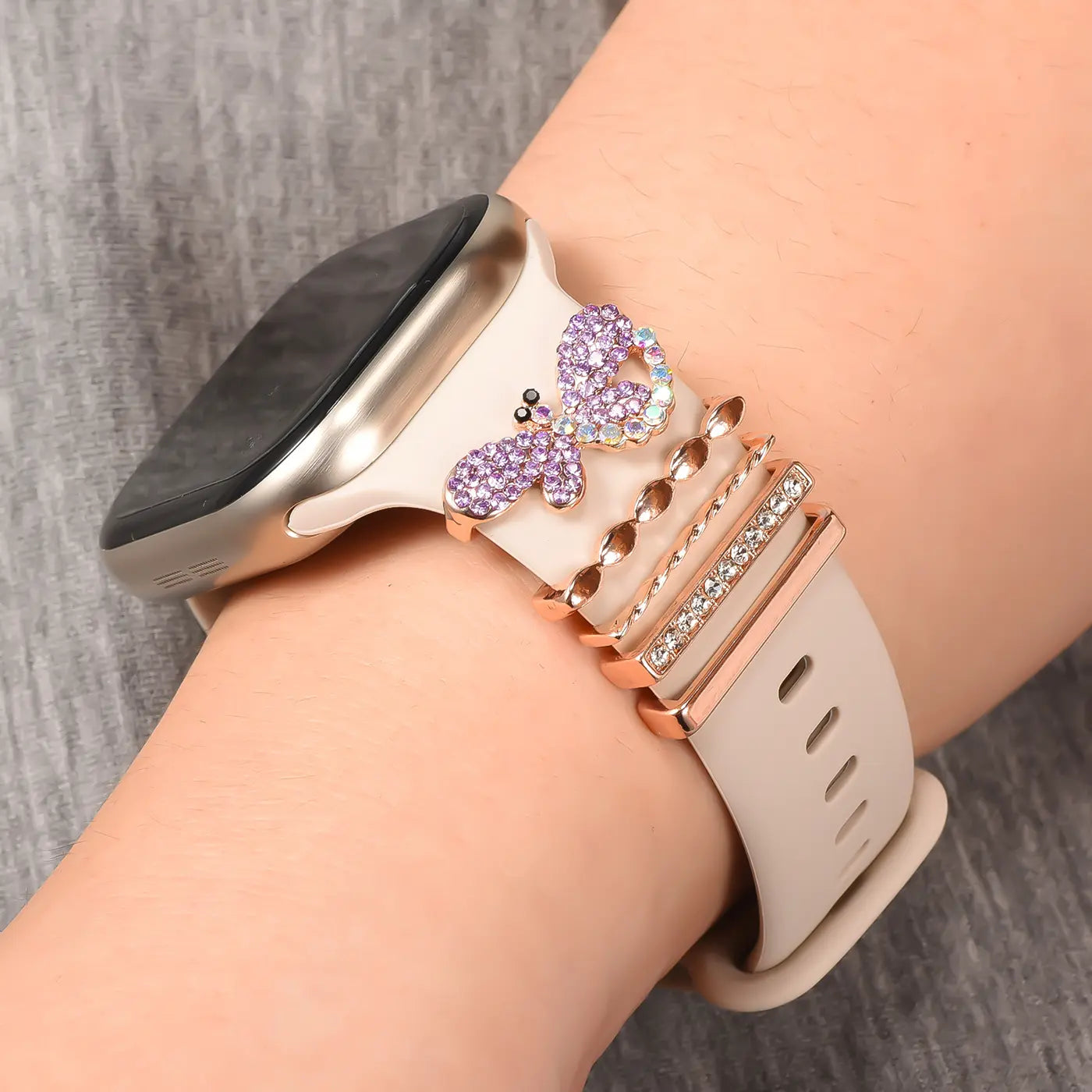 Smartwatch-Armband mit lila Schmetterlings-Charm und roséfarbenen Ringen, Nahaufnahme.