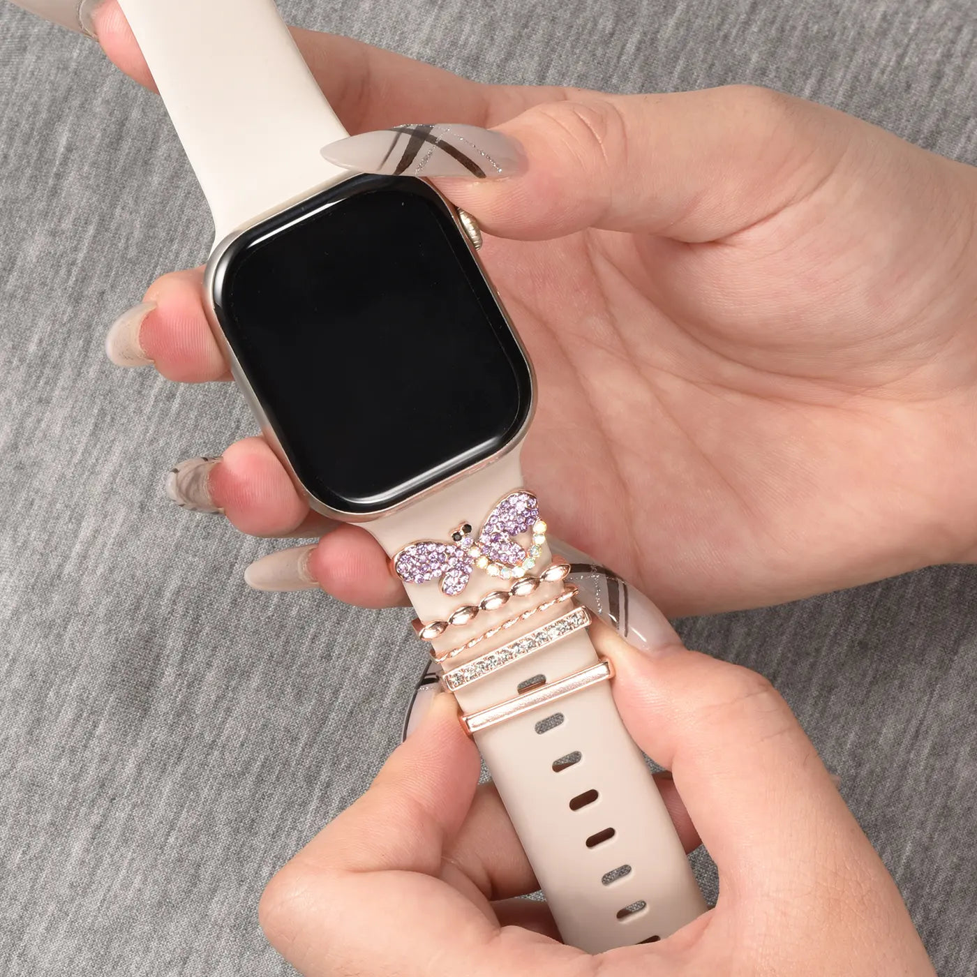 Hände befestigen lila Schmetterlings-Charm an beige Smartwatch-Armband aus Silikon.
