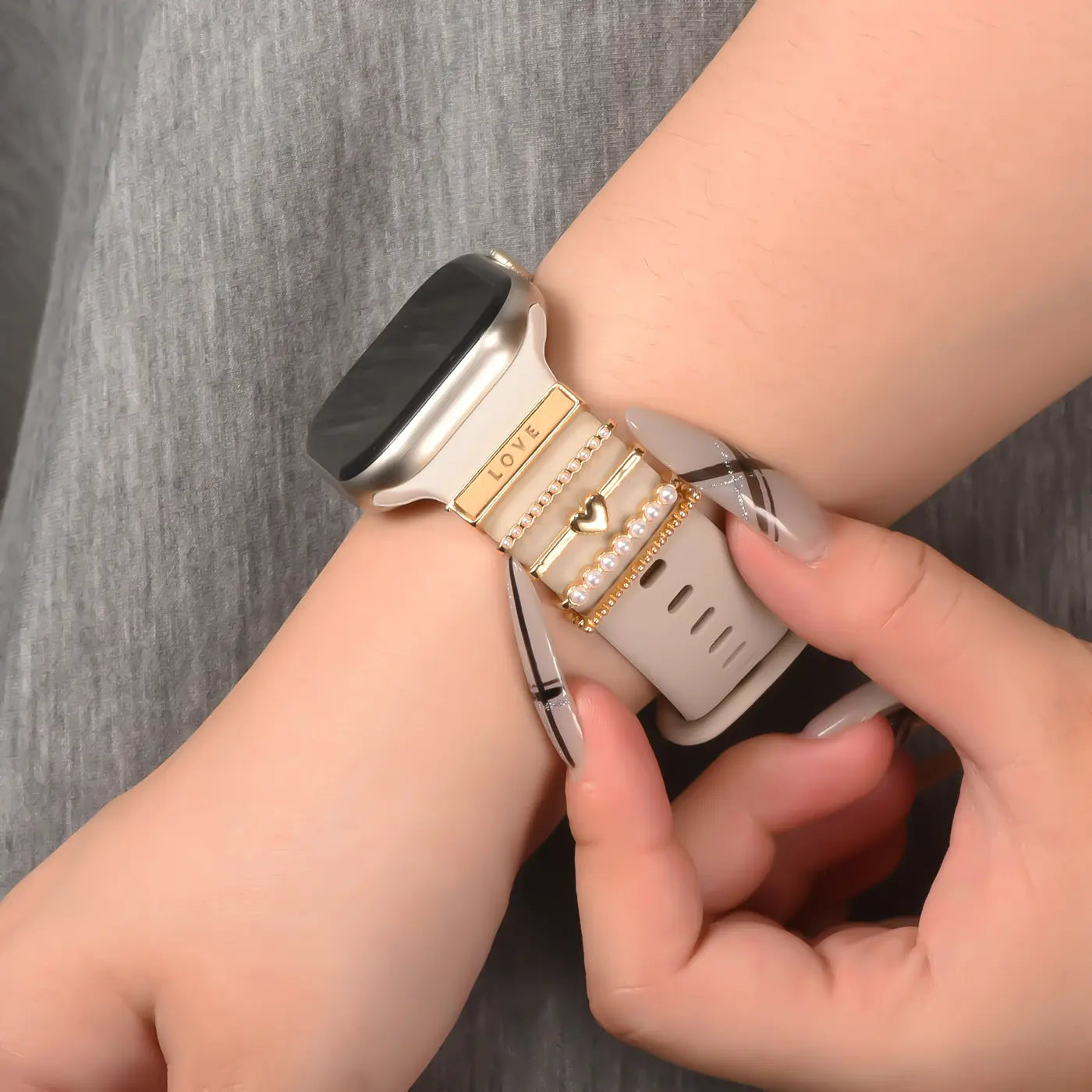 Goldfarbener Smartwatch-Armbandschmuck mit Herz-Anhänger und Perlen, auf hellem Band.