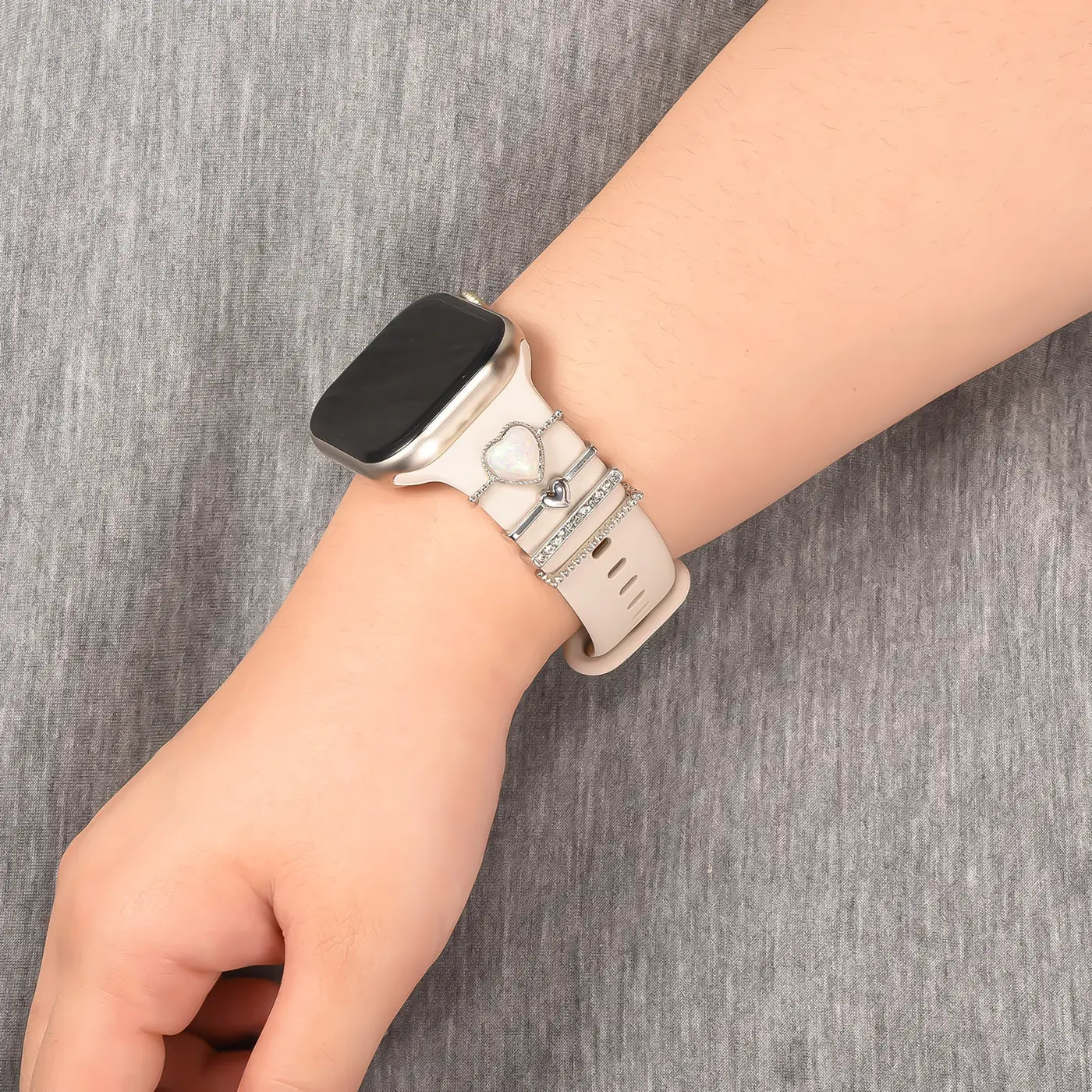 Helles Smartwatch-Armband aus Silikon mit silbernen Charms (Herz, Ringe) an einem Handgelenk.