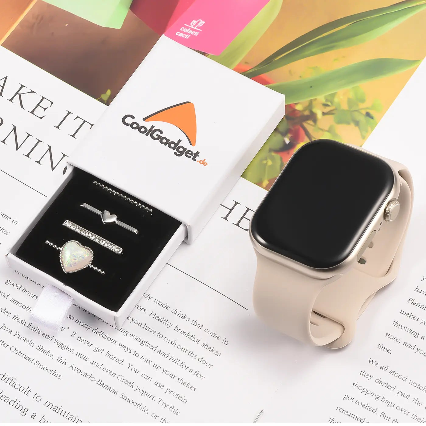 Silberne Smartwatch-Armbandschmuck-Ringe mit Herz-Motiv in Schachtel, neben heller Smartwatch.