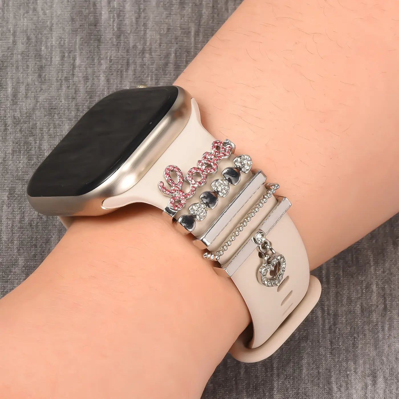 Beige Smartwatch-Armband mit rosa "Love"-Schriftzug und silbernen Charms, Nahaufnahme.