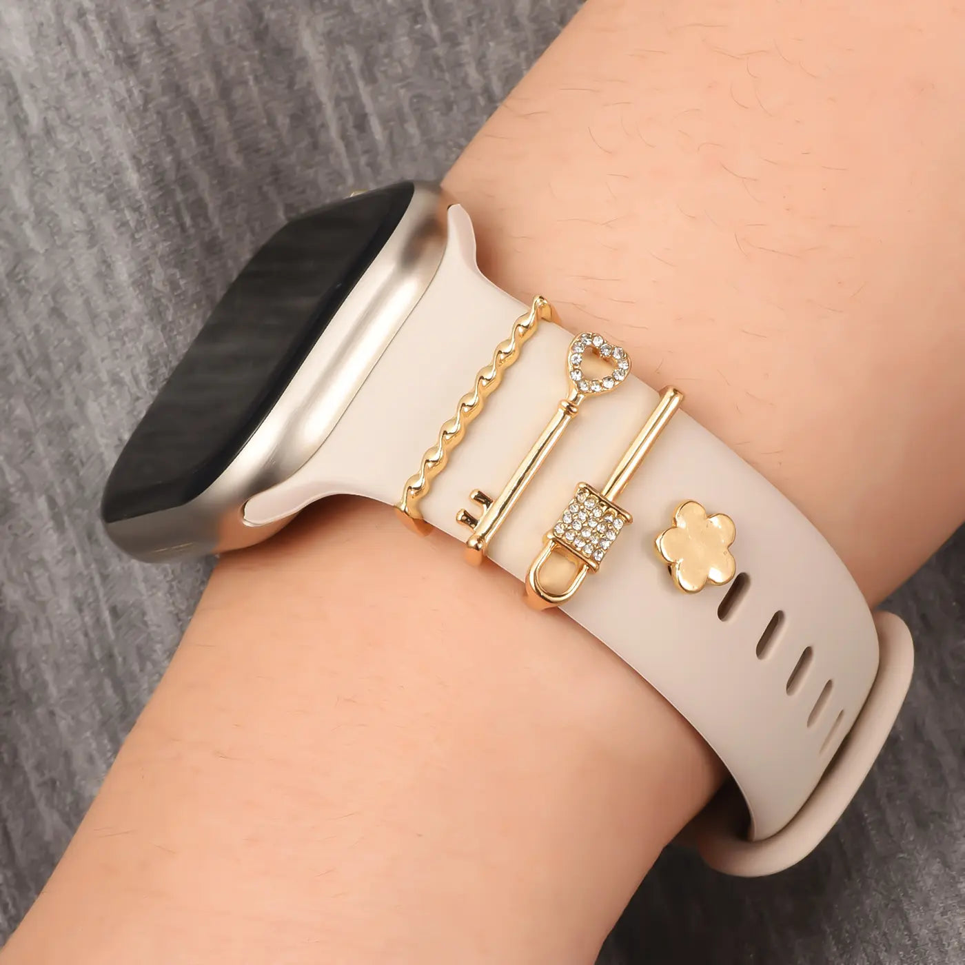 Smartwatch-Armband aus hellem Material mit goldenen Charms: Schlüssel, Herz, Blume. Nahaufnahme.