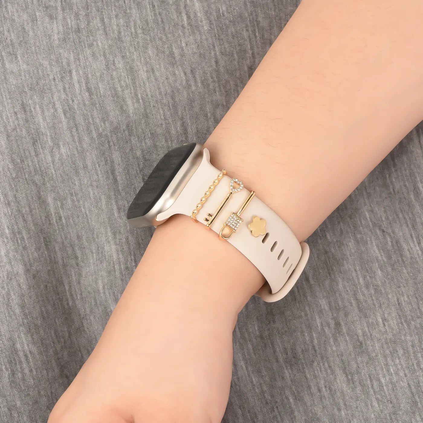 Beiger Smartwatch-Armband mit goldenen Charms (Herz, Pfeil, Kleeblatt), Nahaufnahme.