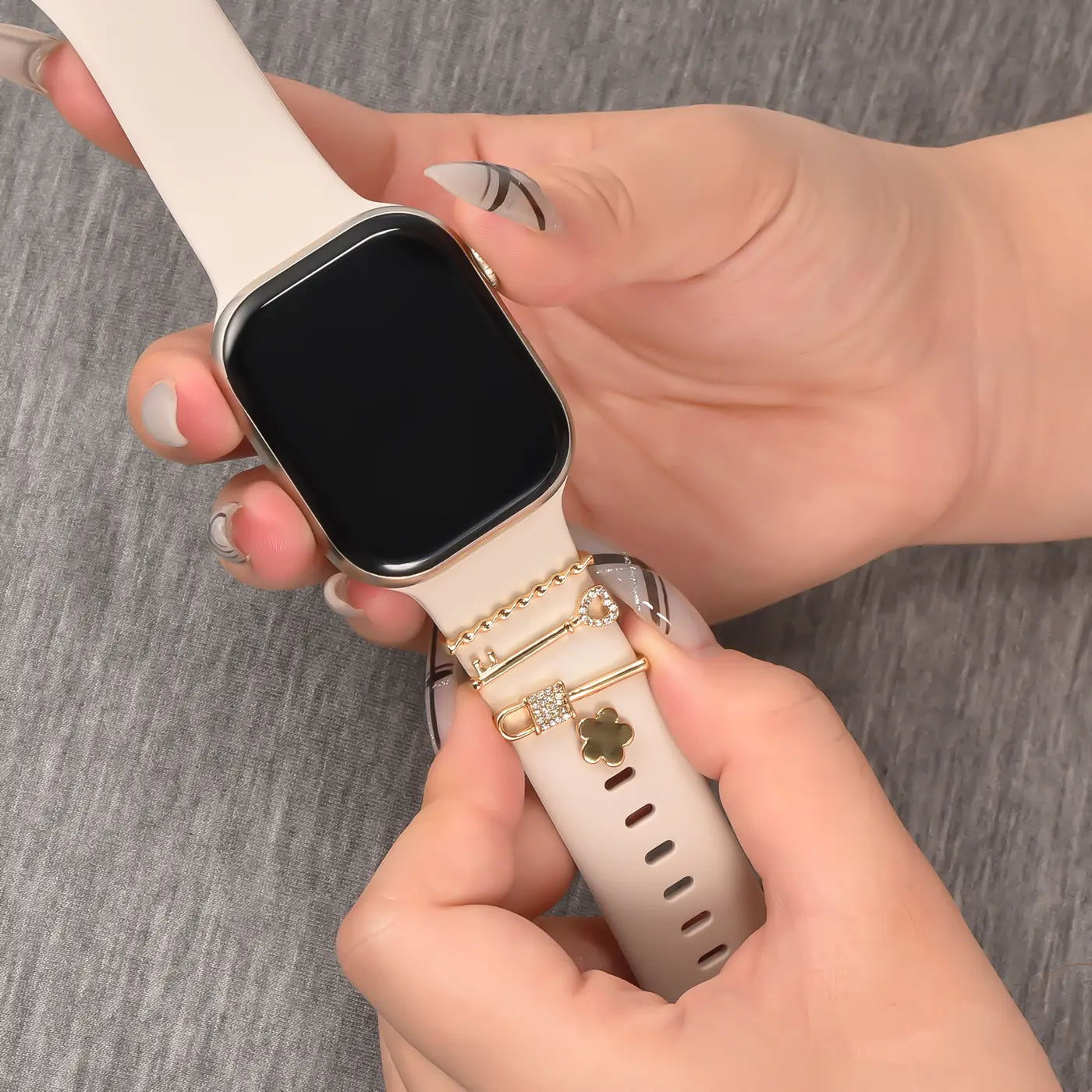 Hände mit Smartwatch, beige Armband, goldene Charms (Schloss, Blume) von vorne