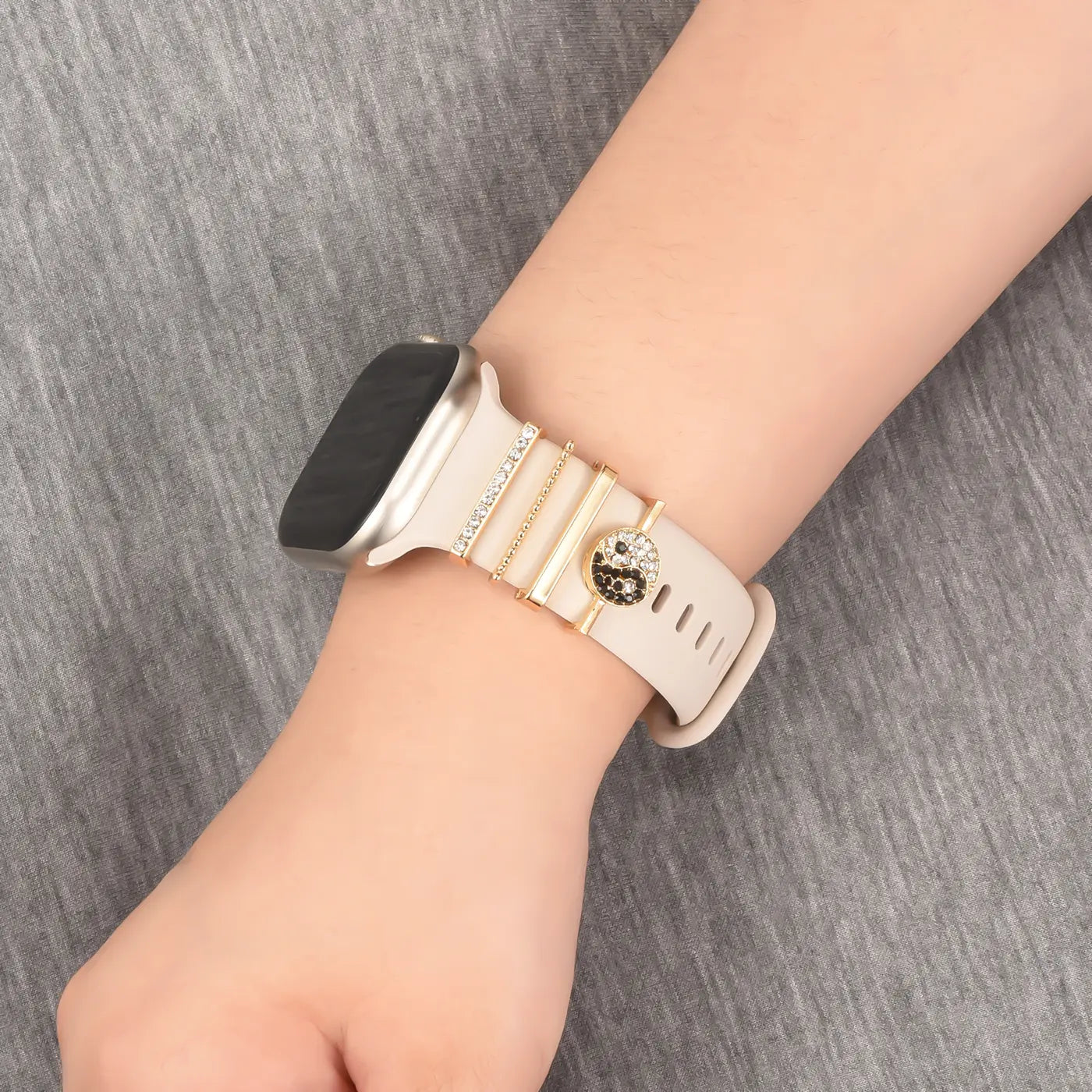 Beige Smartwatch-Armband mit goldfarbenen Charms, darunter ein Yin-Yang-Symbol.