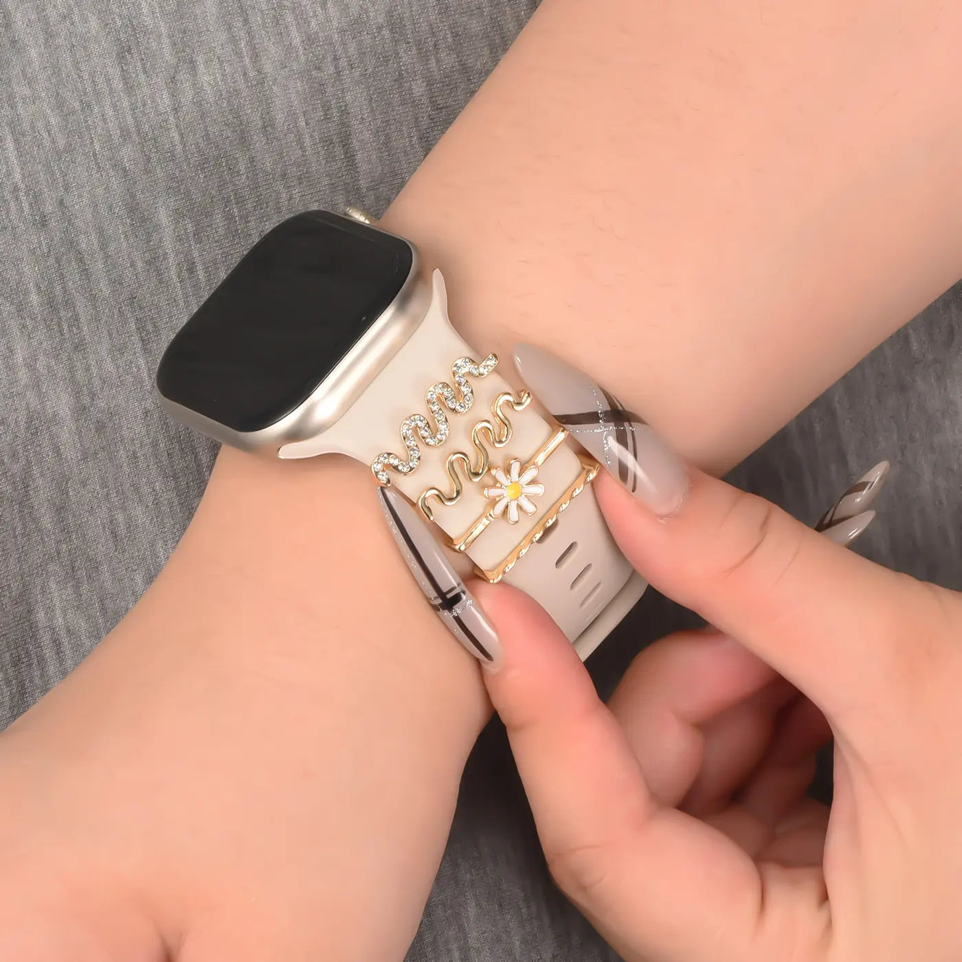 Smartwatch-Armband aus hellem Material mit goldenen Charms, Nahaufnahme von der Seite.