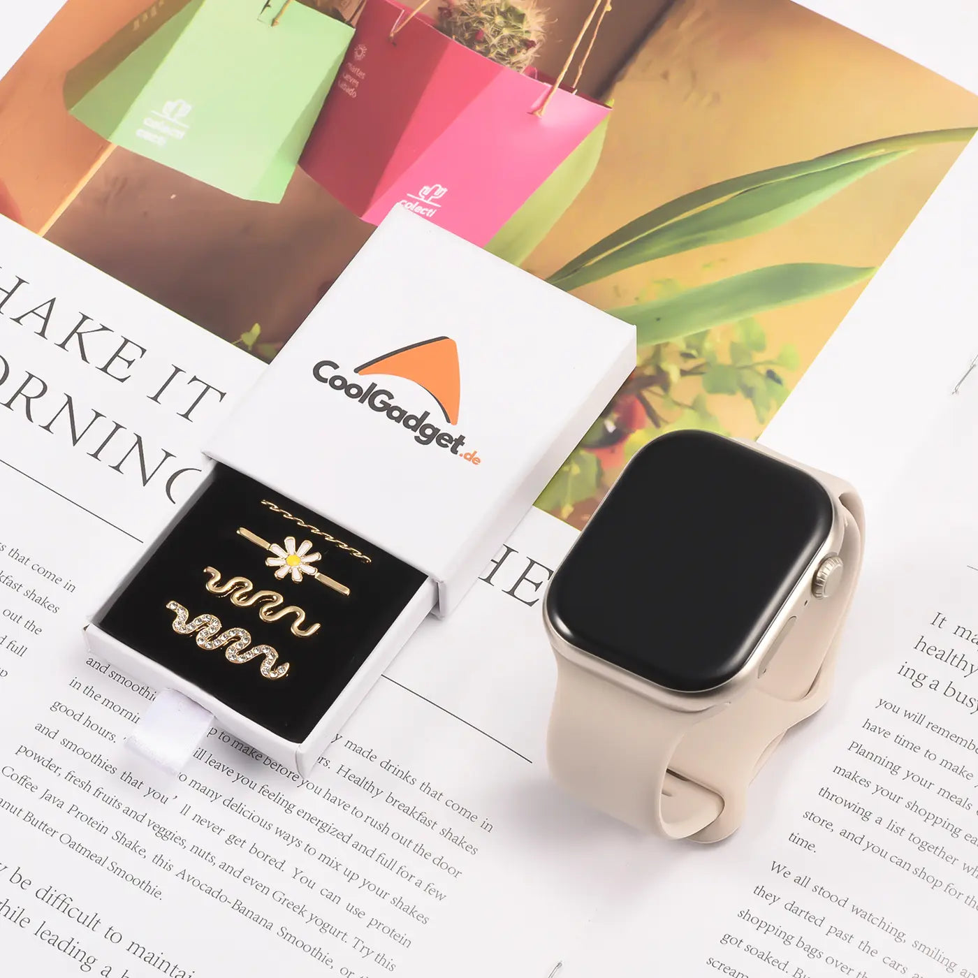 Goldfarbener Smartwatch-Schmuck mit Blumen- und Schlangen-Motiven in Box, neben heller Smartwatch.