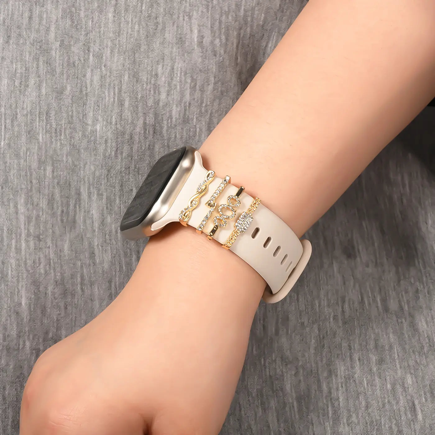 Goldfarbener Smartwatch-Armbandschmuck mit Charms auf weißem Band, Nahaufnahme.