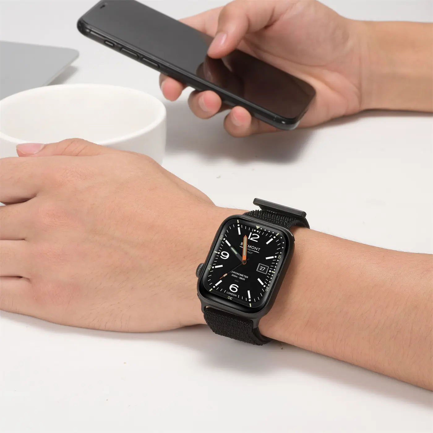 Nahaufnahme: Schwarzes Nylon-Fitnessarmband an einer Apple Watch am Handgelenk, Person hält ein Smartphone.