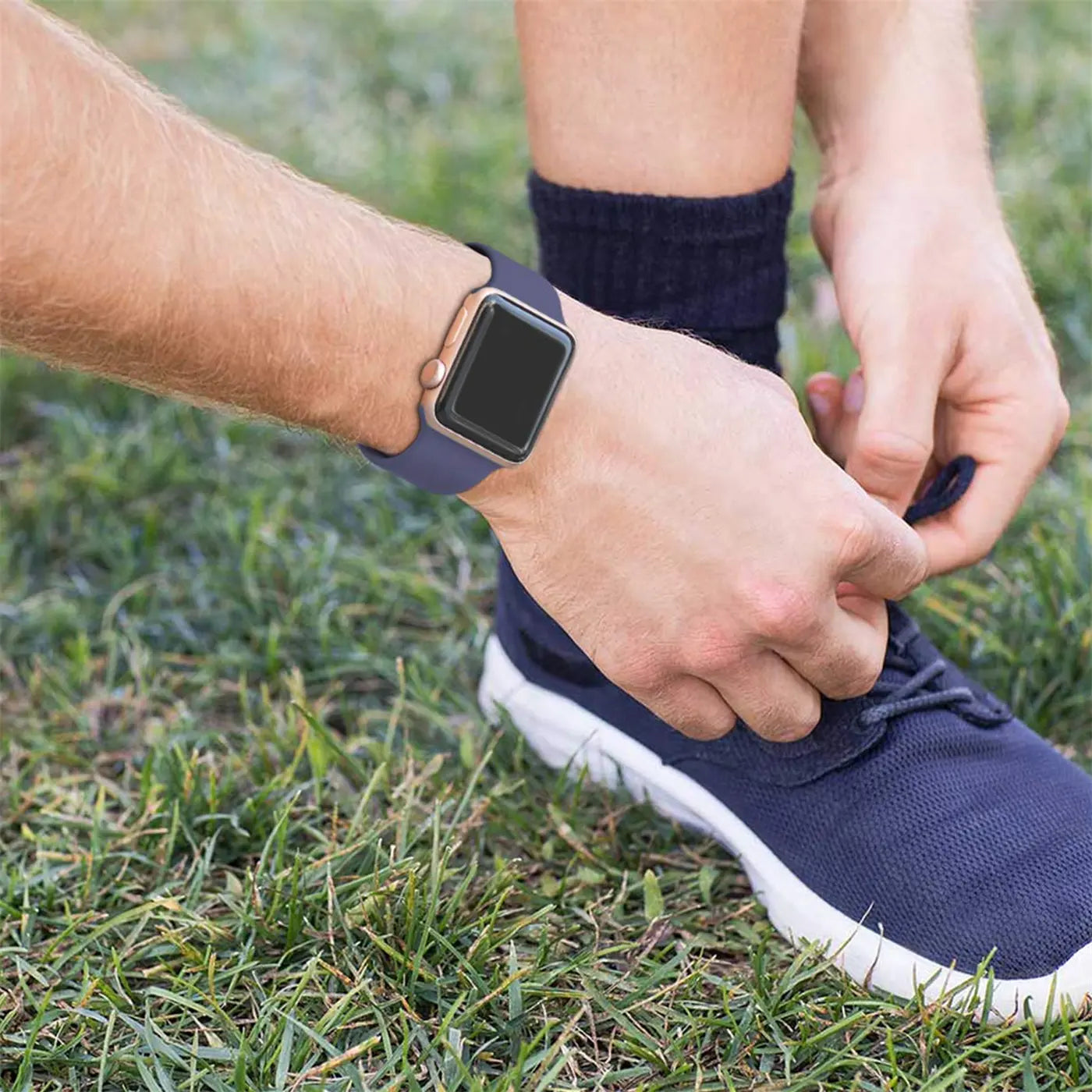 Nahaufnahme: Arm mit dunkelblauem TPU-Fitnessarmband an einer Apple Watch, Person bindet Schnürsenkel.