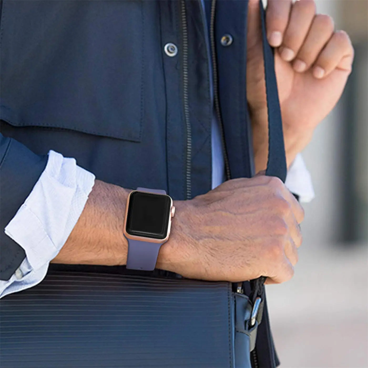 Nahaufnahme eines Arms mit goldener Apple Watch und lila TPU-Armband, das eine dunkelblaue Tasche hält.