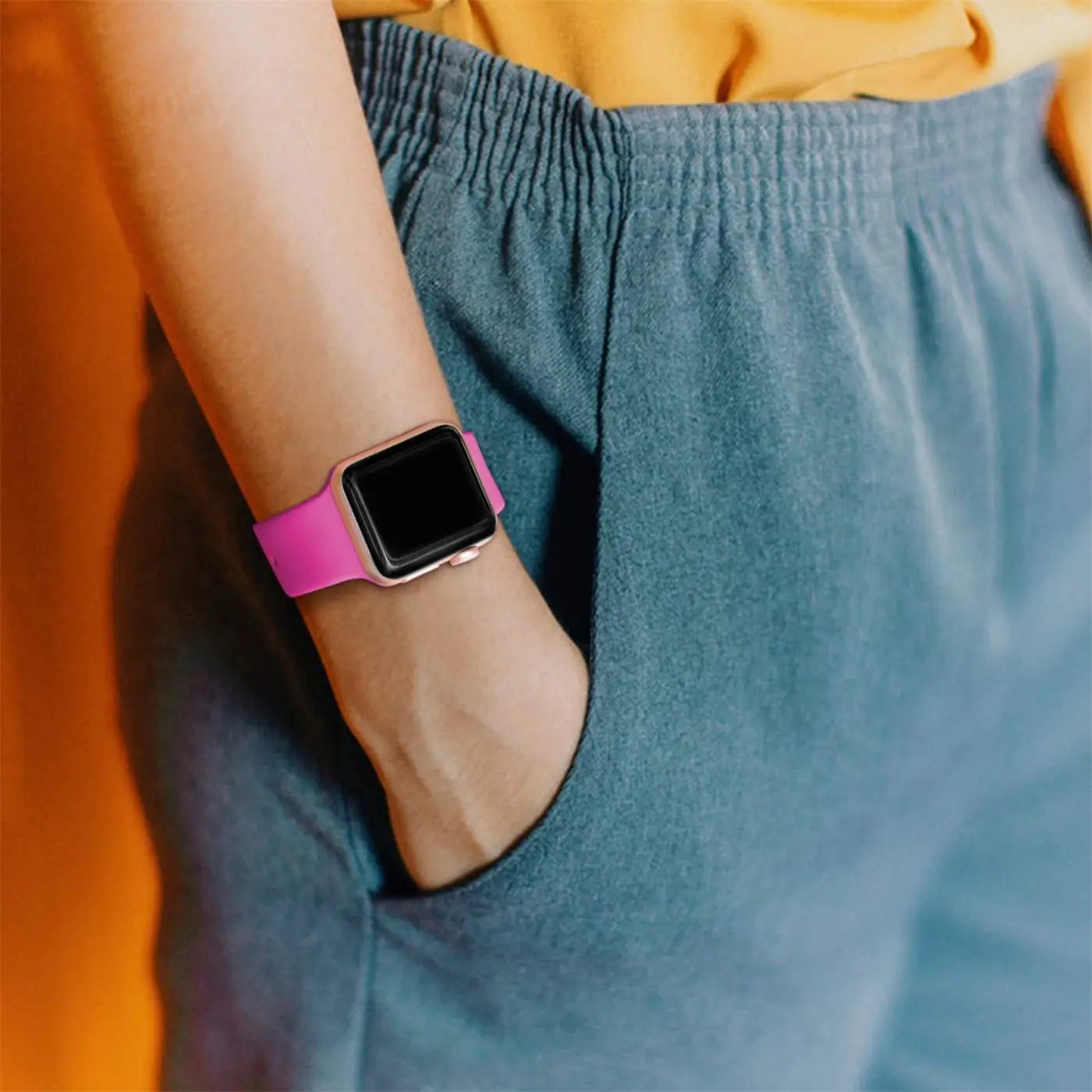 Nahaufnahme: Pinkes TPU-Fitnessarmband an einer Apple Watch am Handgelenk einer Person, die die Hand in der Hosentasche hat.