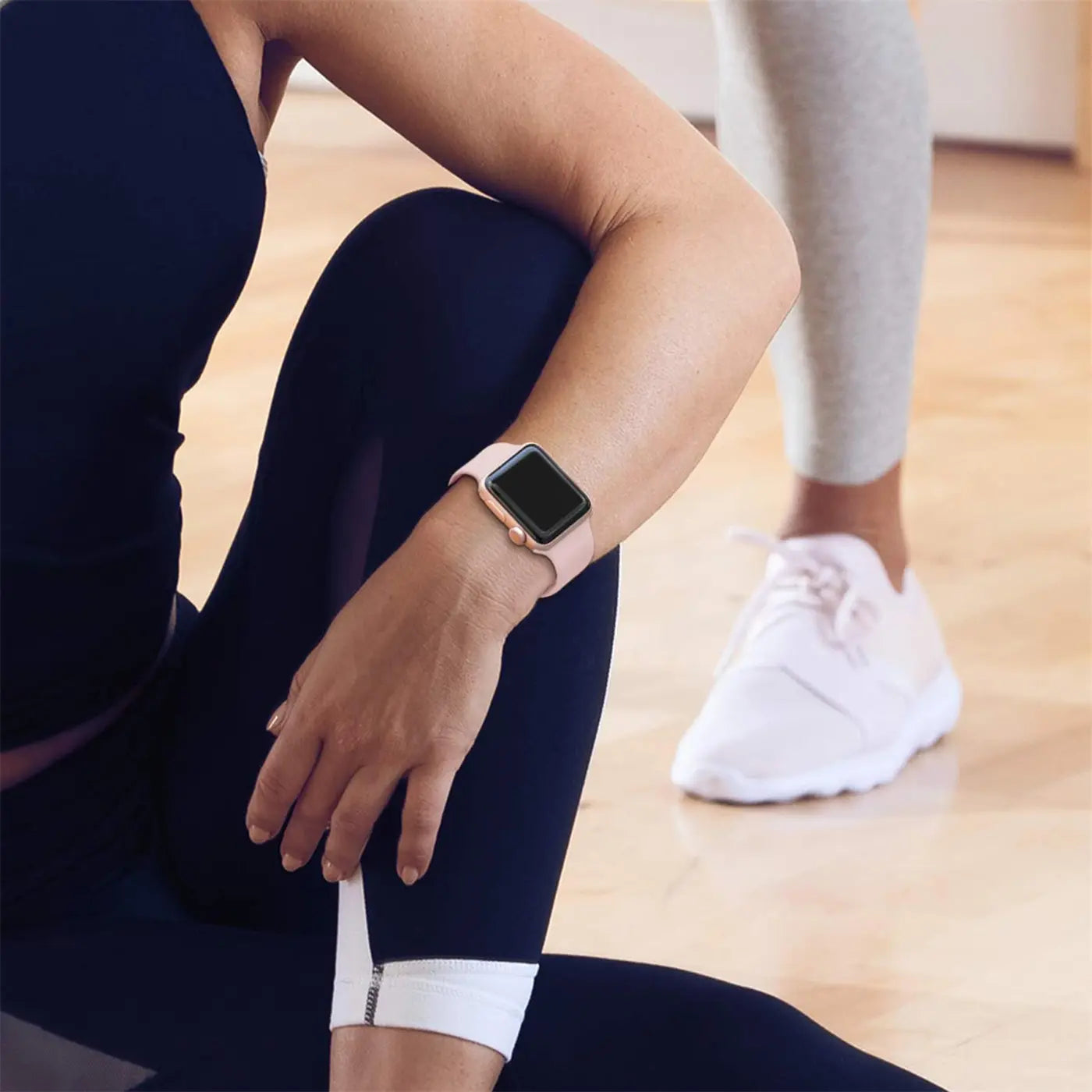 Frau trägt rosafarbenes TPU-Fitnessarmband mit goldener Apple Watch am linken Handgelenk, Seitenansicht.