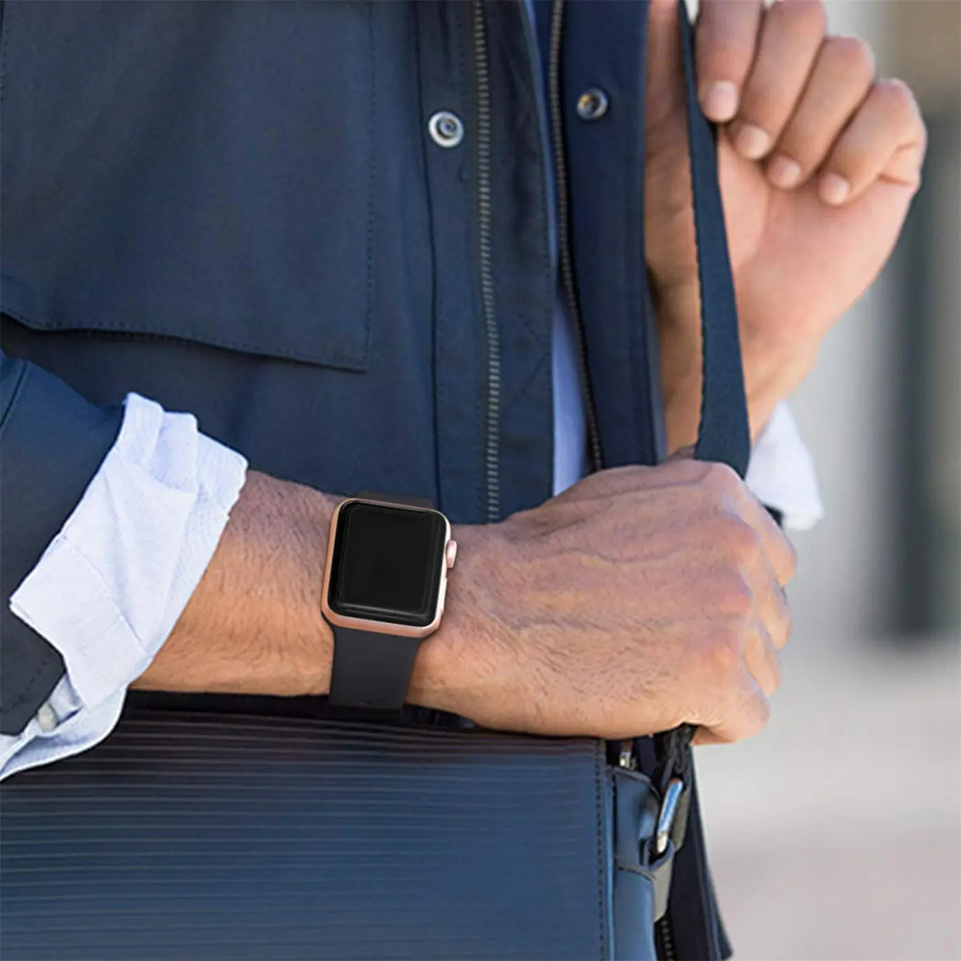 Nahaufnahme eines Arms mit roségoldener Apple Watch und schwarzem TPU-Armband, das eine schwarze Tasche hält.