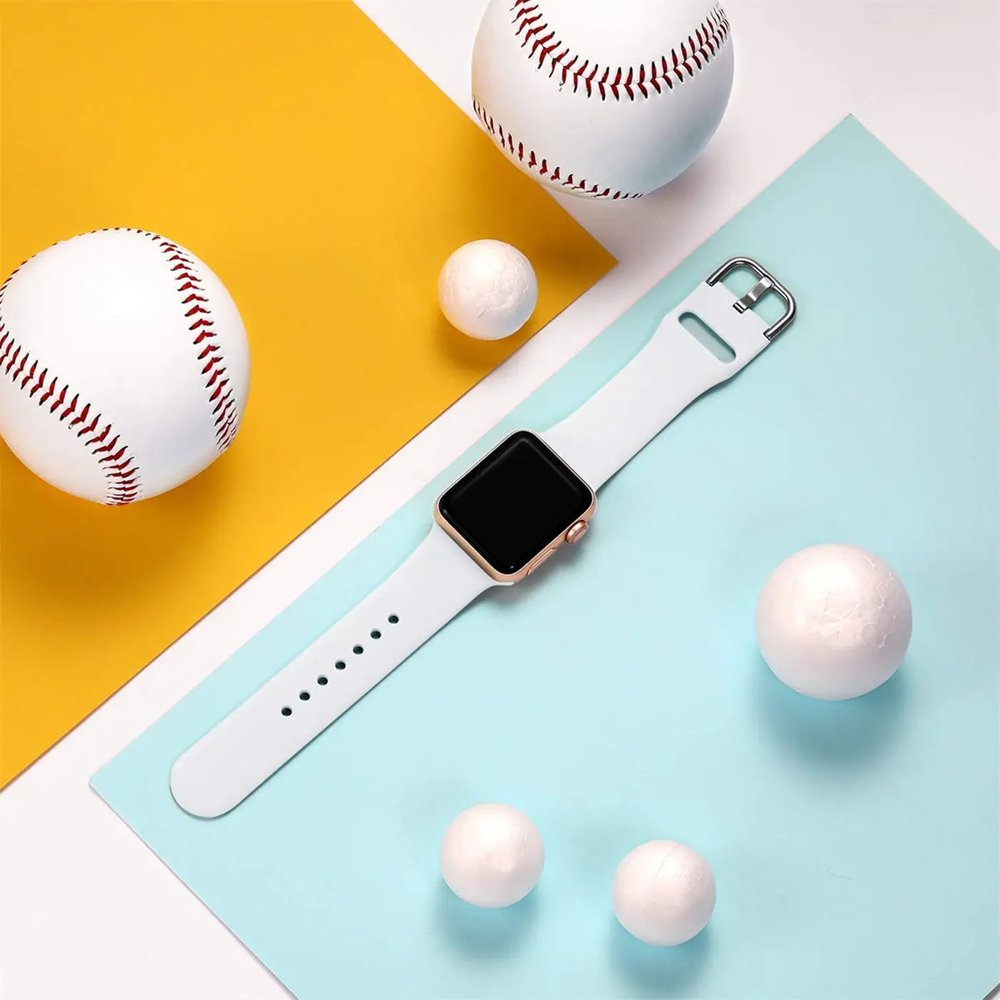 Apple Watch mit roségoldenem Gehäuse und weißem TPU-Armband, von oben auf gelb-blauem Hintergrund mit Bällen.