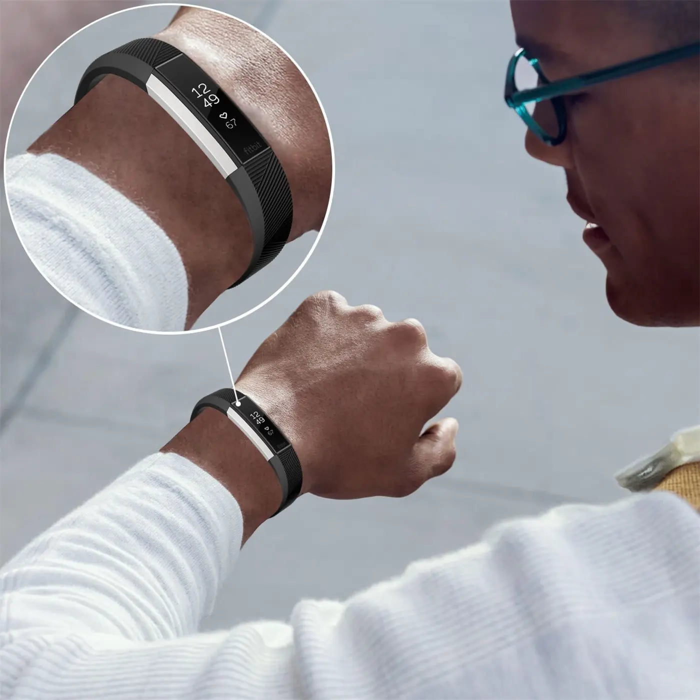 Mann mit schwarzem Fitbit-Armband und silbernem Tracker am Handgelenk, von hinten rechts gesehen. Detailansicht des Trackers.