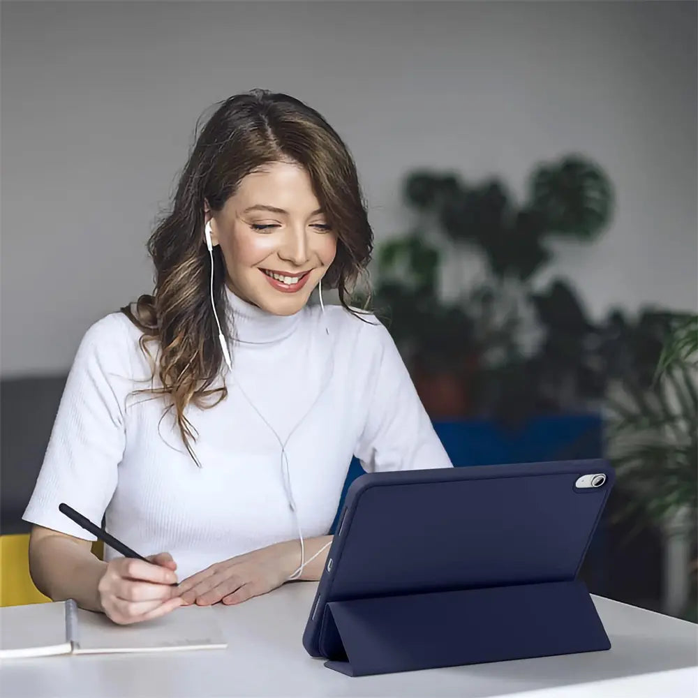 Frau mit Kopfhörern schreibt Notizen, während ein dunkelblaues 13" iPad Pro (M4) in einer Smart Cover Hülle auf dem Tisch.