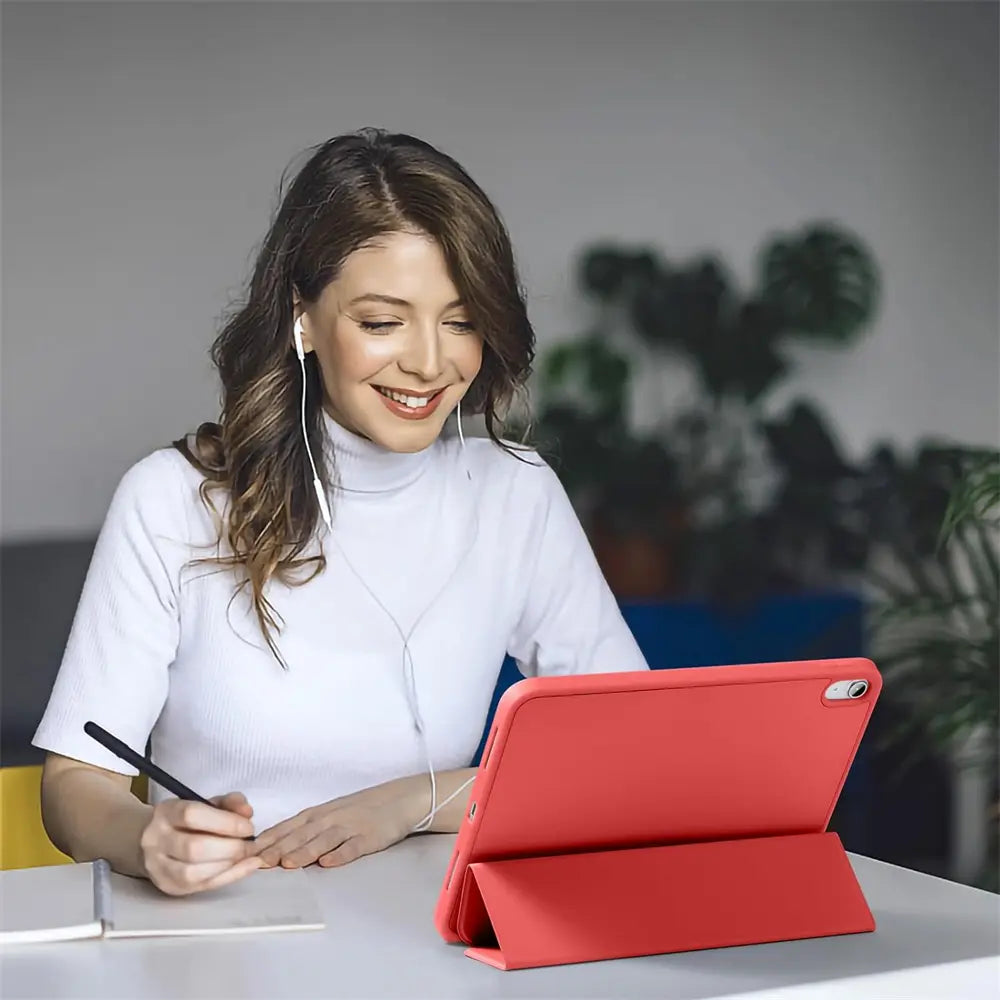 Frau mit Kopfhörern schreibt mit Stift, während ein rotes 13" iPad Air/Pro (M3/M4) in einer Smart Cover Hülle aufgestellt.